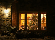 Welcome Home Christmas Tree.Outdoor Close Up View Of Old Style Brick House Window With Decorated And Glowing Christmas Tree. Night Scene. Christmas And New Year Holiday Background. 