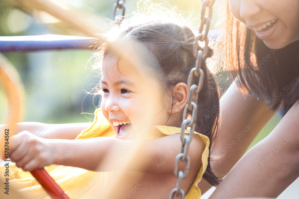 Happy asian little child girl having fun to ride on swings when mother ...