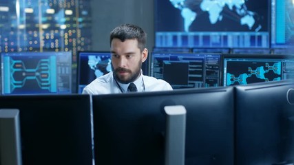 Fototapete - In the System Control Center Technical Operator Monitors Displays at His Workstation. He's Surrounded by Displays Showing Relevant Data. In the Background Data with Interactive Map. 