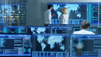 Fototapete - In the System Monitoring Room Two Senior Operators Work on a Big Interactive Map. Facility is Full of Screens Showing Technical Data. Shot on RED EPIC-W 8K Helium Cinema Camera.
