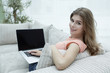 © ASDF - beautiful young woman working with laptop sitting on sofa and looking at camera.