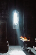 A Dark Background Of Old Armenian Christian Church Monastery Interior With A Sun Ray Falling To The Candles From A Window. Abstract Christian Religion Belief And Travel Concept.