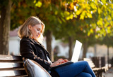 Fototapeta  - Woman using laptop in the city street under colorful autumn trees