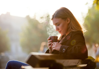 Woman smelling and drinking hot coffee, autumn sunset at the street