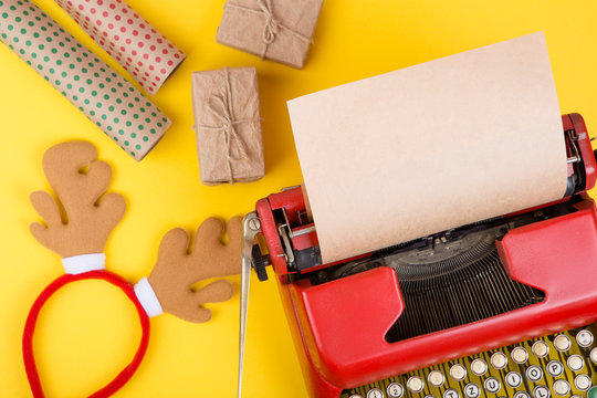Holidays concept - red typewriter with blank craft paper, gift boxes on yellow background