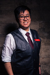 Young transgender man in semi formal clothing with a bondage style leather vest poses in a grungy urban location