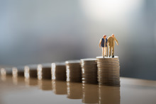 Concept Of Retirement Planning. Miniature People: Old Couple Figure Standing On Top Of Coin Stack.