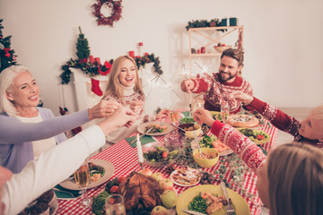 Wall Mural - Cheerful relatives sit and celebrate with sparkles up gathered together, setted festive desktop with tasty food, married couple, siblings, granny, in knitted traditional x mas costumes