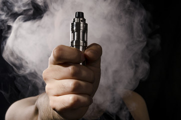 man holding electronic cigarette or vape device with smoke at the background.