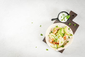 Healthy food snack. Tortillas taco with grilled chicken, avocado, fresh salsa, lettuce, lime. With yogurt & parsley sauce. On light gray stone marble table, wooden cutting board. Top view copy space