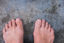 Empty Bare Feet Of Elderly Men Standing On Black Concrete Floor.