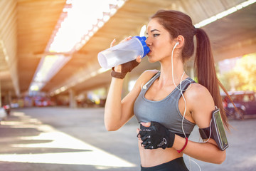 Sportswoman drinking water after sports training outdoors.