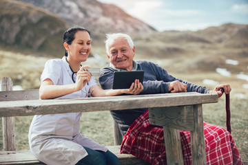 Canvas Print - Smiling caregiver nurse and  disabled senior patient using digital tablet and credit card outdoor