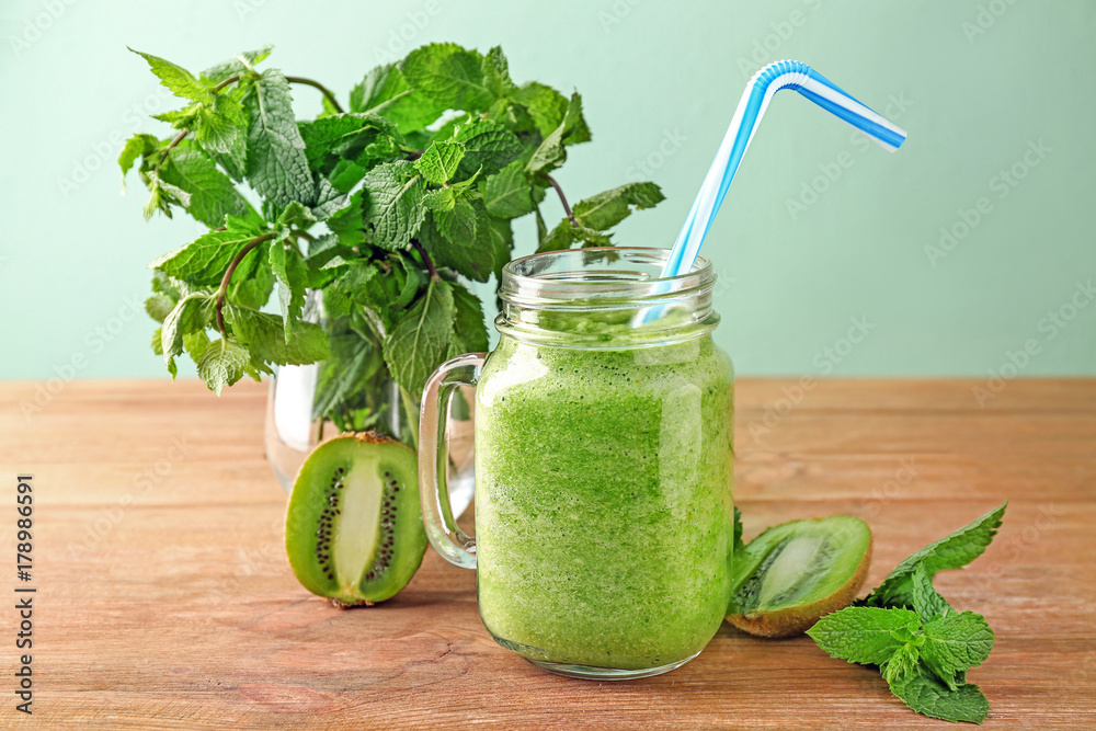 Delicious kiwi smoothie with mint in mason jar on table against color background