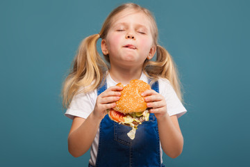 Wall Mural - Adorable cute little girl in white shirt and jean jumpsuit with hamburger