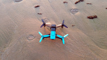 Black And Blue Drone Standing On The Sand, View From Above