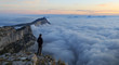 A man looking over a sea of clouds in the mountains at dawn. Vercors, France.