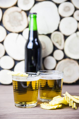 Dark beer in a bottle and light in glasses on a wooden table next to salty snacks - chips, peanuts and crackers