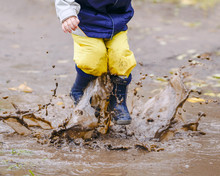 Happy Child Jumping On Puddles In Rubber Boots
