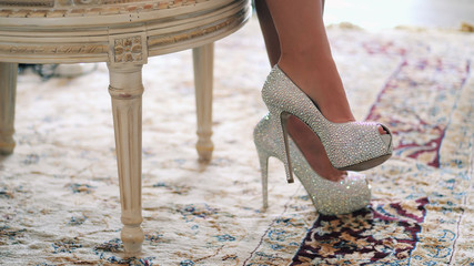 Beautiful sexy legs of young bride. Woman wearing shining heels with crystals and sitting in luxury restaurant.