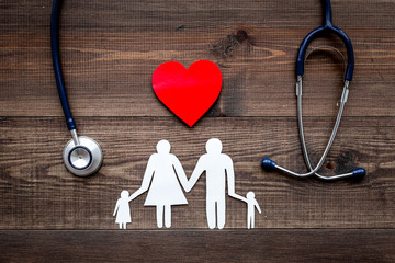 take out health insurance for family. stethoscope, paper heart and silhouette of family on wooden ba