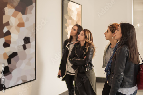 Fotomural Four girl friends looking at modern painting in art gallery