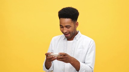 Sticker - Concentrated happy Young african man in shirt playing on smartphone over yellow background