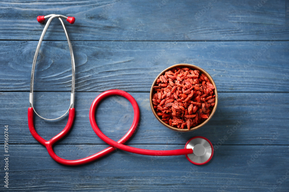 Bowl with goji berries and stethoscope on wooden background