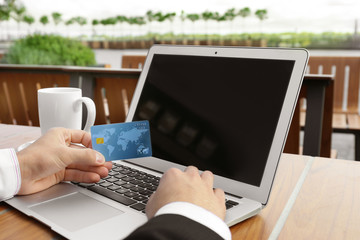 Poster - Young man using laptop and credit card for online shopping at table