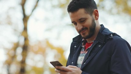 handsome confident man using holding smart phone mobile nodding head agreement agree glad satisfied guy chatting conversation online social networking checking good news outside autumn park blur trees