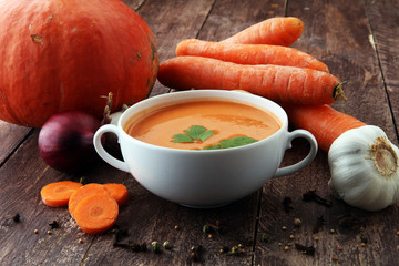 Pumpkin and carrot soup with cream and parsley on dark wooden background.