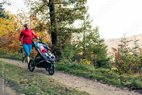 Fotografia, Obraz Running mother with stroller enjoying motherhood at autumn sunset