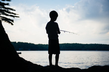 Silhouette Of A Boy Fishing On A Lake At Sunset