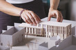 © BONNINSTUDIO/Stocksy - Close up of hands of young architect working on a building project with a scale model.