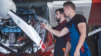 Wall Mural - Two mechanics working on a small aircraft in a hangar with the cowling off the engine as they perform a service or repair