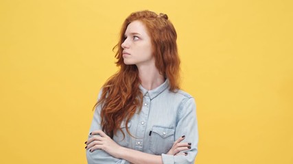 Wall Mural - Offended ginger woman in denim shirt holding crossed arms and looking at the camera over yellow background