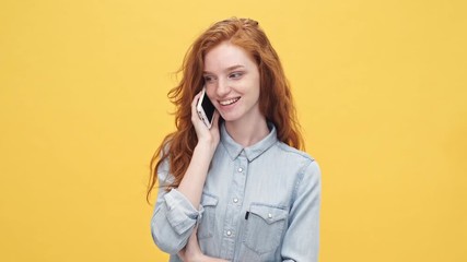 Sticker - Happy ginger woman in denim shirt talking by the smartphone over yellow background