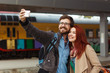 © Ольга Тернавская - Young couple hiking taking selfie with smart phone. Happy young man and woman taking self portrait with travel station in background.