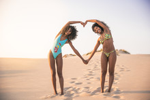 Laughing Girlfriends Showing Heart With Hands On The Beach