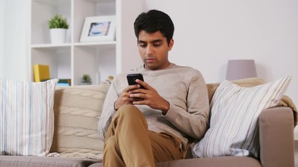 man with smartphone sitting on sofa at home