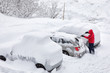 Young attractive man brushing the snow off his car on a cold winter day