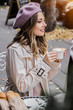 Moments of joy. Side view of beautiful young french woman in beret looking away and smiling while drinking coffee in french vintage cafe. Spending time with best friend. Women drinking coffee.