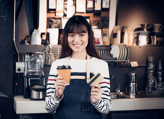 Poster - Woman barista holding coffee to go cup and credit card,asia female waitress using contactless payment in coffee shop business at counter bar in cafe,moder food owner business start up.