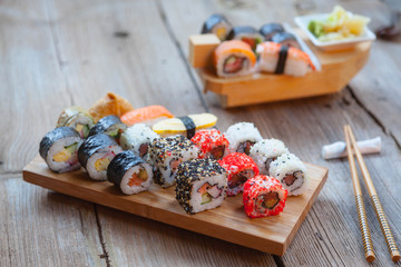 Wall Mural - A variety of sushi on old wooden table. Sushi rolls, nigiri, raw salmon steak, rice, cream cheese, avocado, lime, pickled ginger.