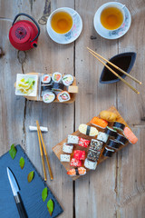 Wall Mural - A variety of sushi on old wooden table. Sushi rolls, nigiri, raw salmon steak, rice, cream cheese, avocado, lime, pickled ginger.