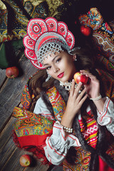 Wall Mural - Girl in folk costume and headdress holding a red Apple in the style fashion on dark wooden background top view