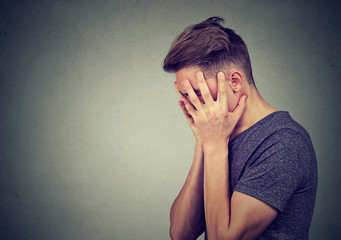 Side profile of a sad young man with hands on face looking down. Depression and anxiety disorder