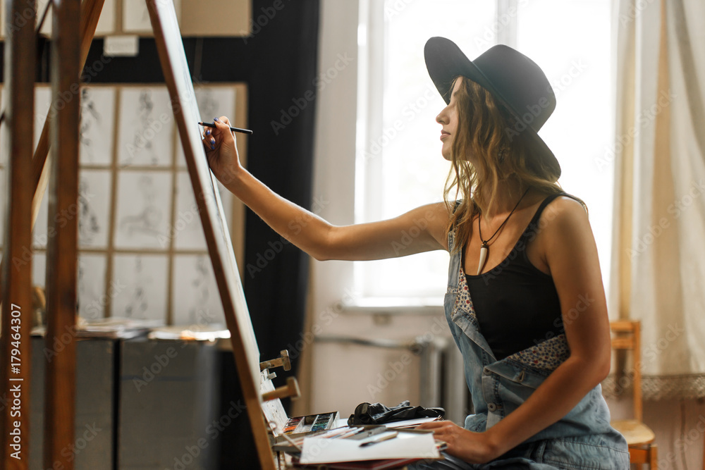 Female artist wears black hat draw picture indoor the studio - obrazy, fototapety, plakaty 