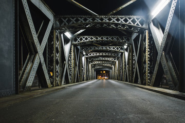asphalt road under the steel construction of a bridge in the city. night urban scene with car light 