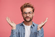 © WHstudio Leushin N - Bearded Caucasian male has hesitatnt and displeased expression, gestures doubtfully, has no answer on difficult question, being puzzled or confused. Uncertain fashionable guy over pink background